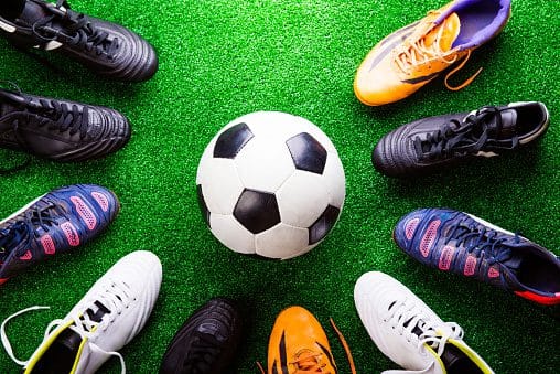 Soccer ball and cleats against artificial turf, studio shot on green background. Indoor and outdoor Soccer Shoes on Turf